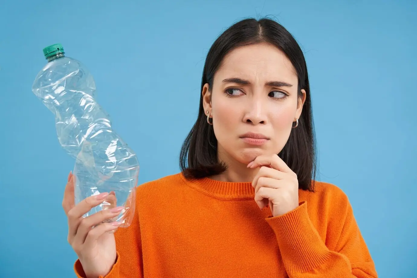 Porträt einer besorgten, nachdenklichen Frau, die auf eine leere Plastikflasche blickt und darüber nachdenkt, wie man sie recyceln kann.